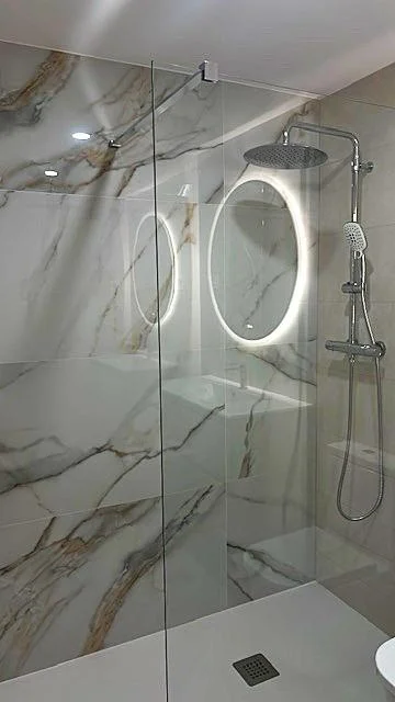 Ducha con revestimiento de mármol veteado y espejo LED ovalado retroiluminado
